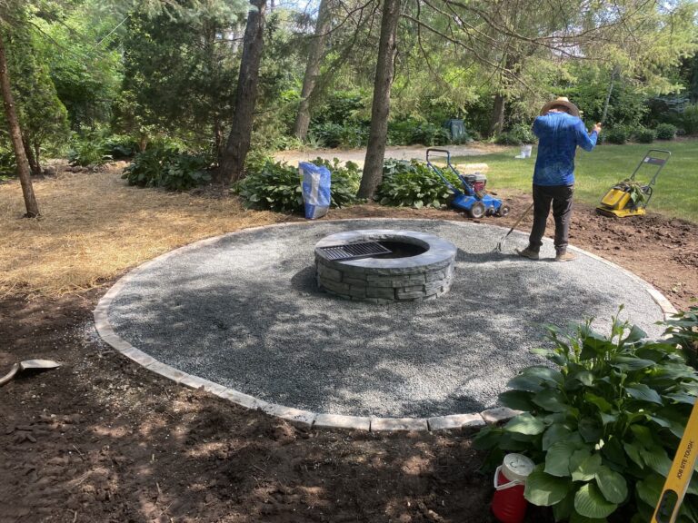 Person landscaping backyard with firepit and gravel.